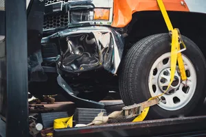 Damaged bumper front fender on pickup truck by car accident carrier on flatbed rollback slide tilt tray of tow truck with yellow ratchet strap tie down, collision, insurance claim concept, Texas. USA